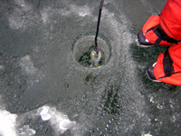 Monitoring team sampling water through a hole in lake ice